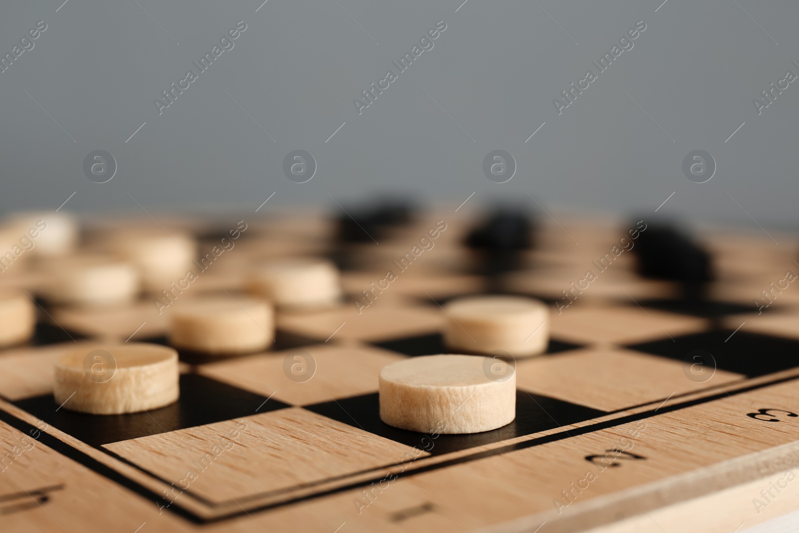 Photo of Wooden checkerboard with game pieces on light grey background, closeup