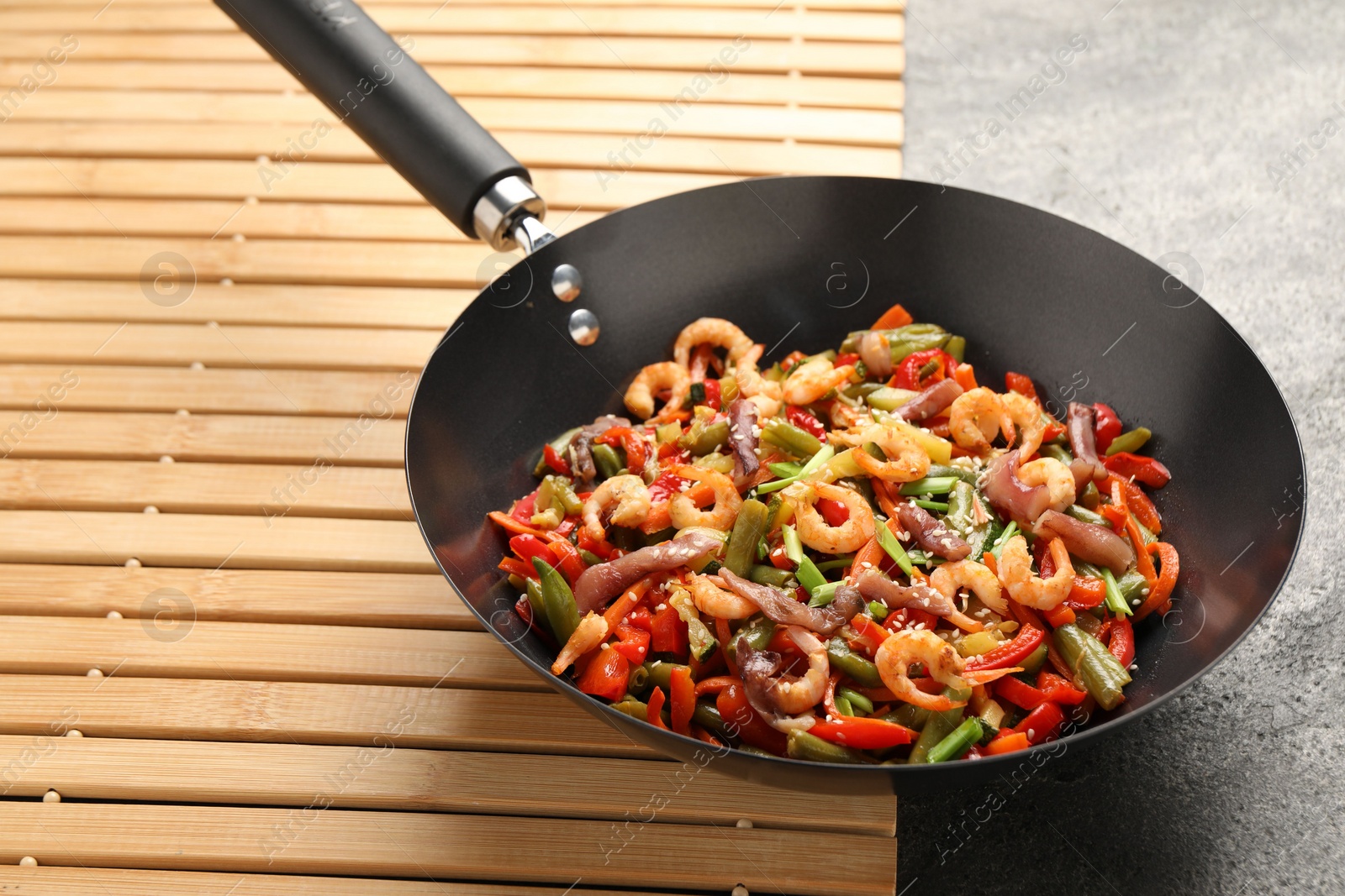 Photo of Shrimp stir fry with vegetables in wok on grey table