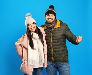 Happy young couple in warm clothes on blue background. Winter vacation