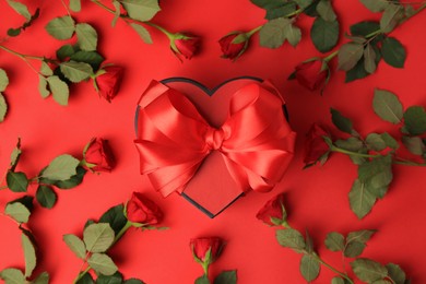 Photo of Heart shaped gift box with bow and beautiful roses on red background, flat lay