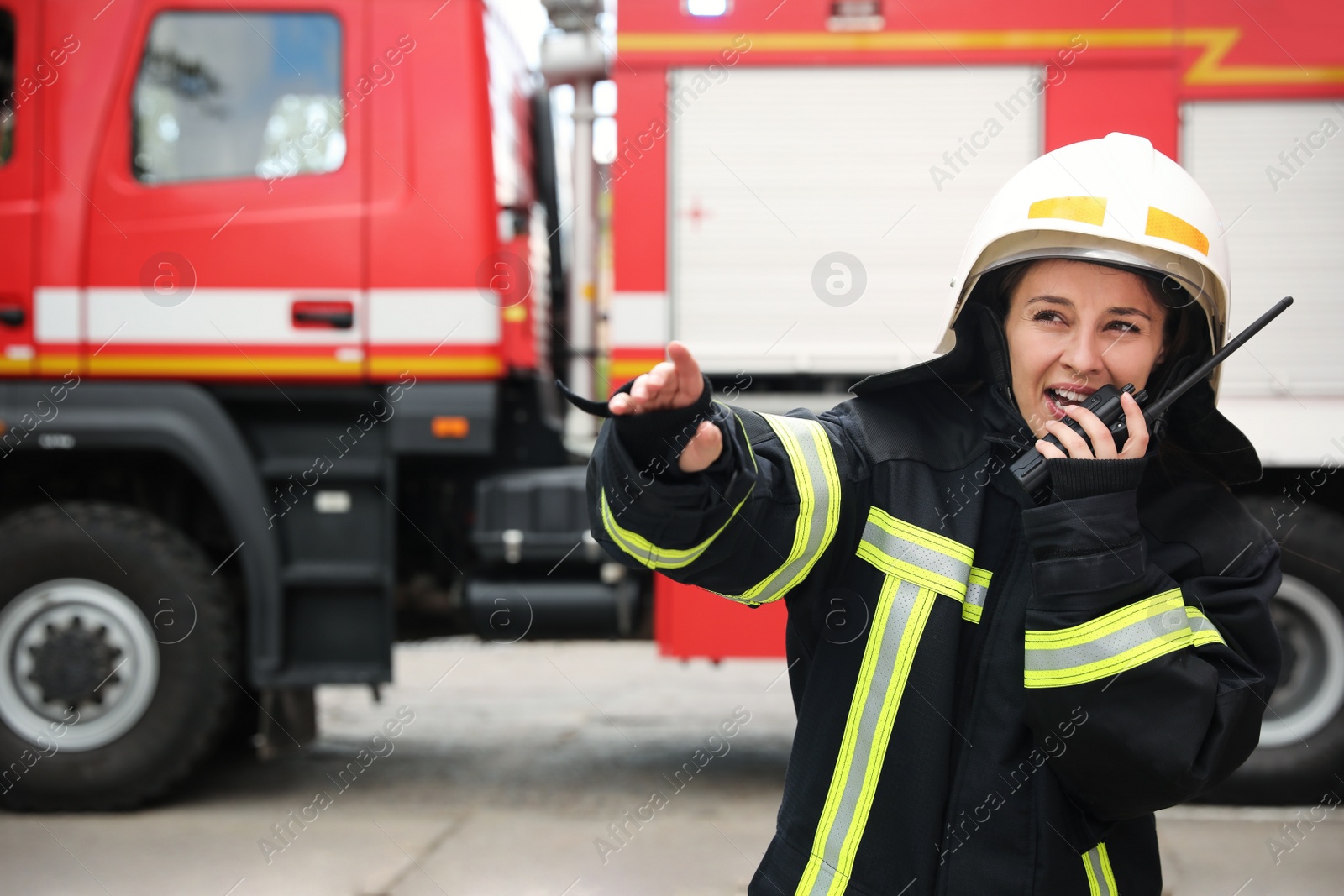 Photo of Firefighter in uniform using portable radio set near fire truck outdoors