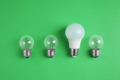Photo of LED light bulb and simple ones on green background, flat lay. Energy saving concept