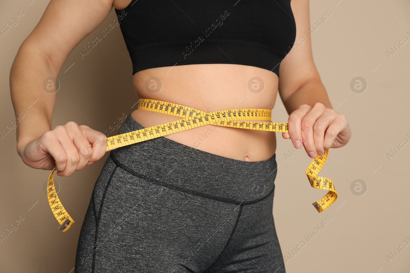 Photo of Woman measuring waist with tape on beige background, closeup