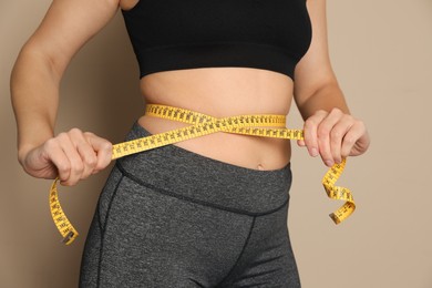 Woman measuring waist with tape on beige background, closeup