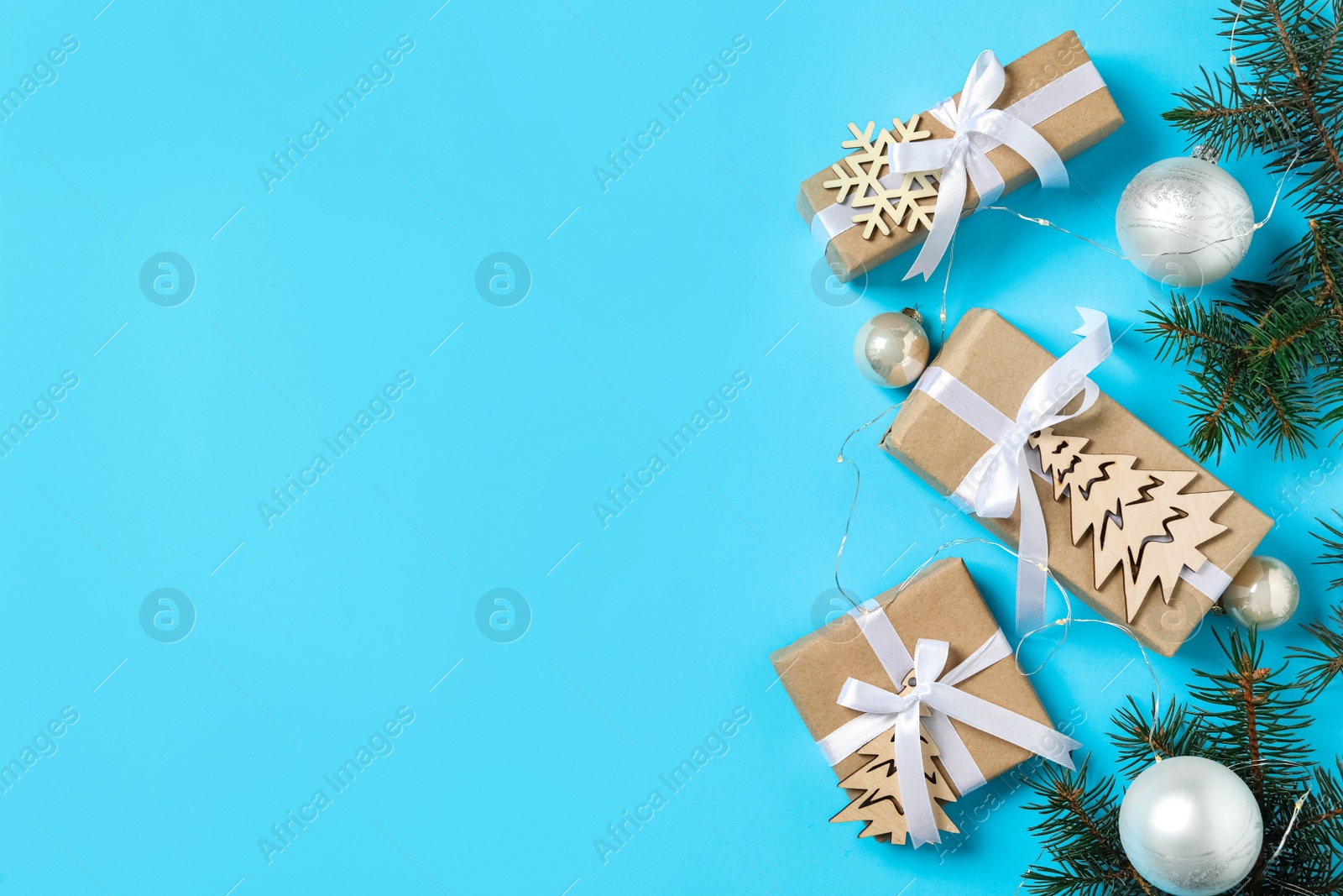 Photo of Gift boxes with Christmas balls and fir branches on light blue background, flat lay. Space for text