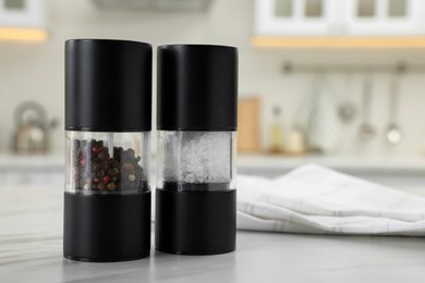 Photo of Salt and pepper mills with napkin on white marble table in kitchen. Space for text
