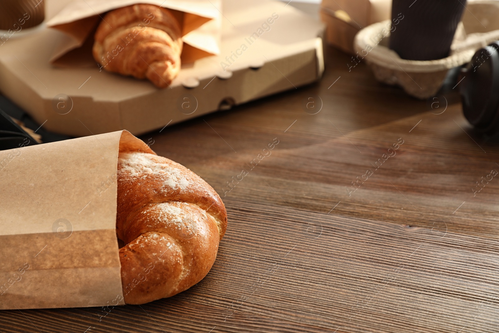 Photo of Paper bag with pastry and takeaway food on wooden table. Space for text