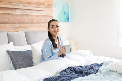 Photo of Woman with cup of hot drink in large bed at home. Elegant interior