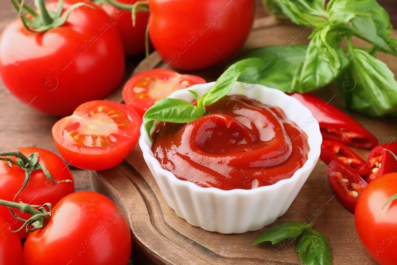 Photo of Bowl of tasty ketchup and ingredients on wooden table, closeup