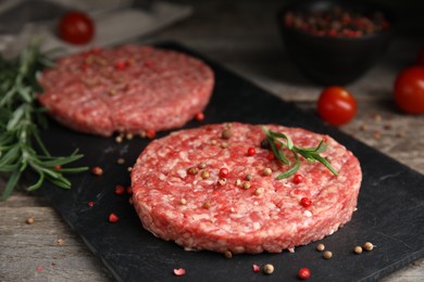 Photo of Raw hamburger patties with rosemary and peppercorns on wooden table, closeup