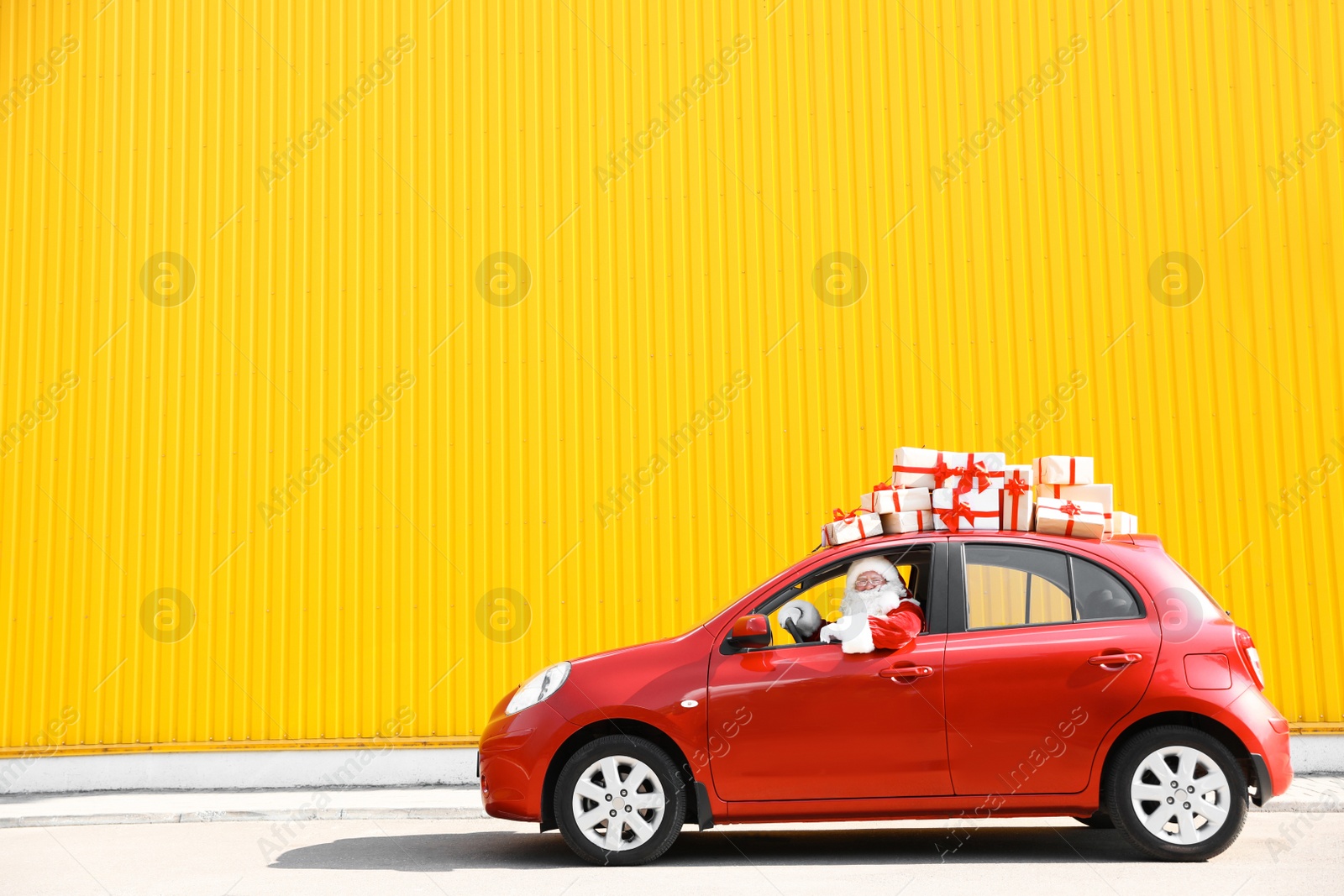 Photo of Authentic Santa Claus driving red car with gift boxes, view from outside