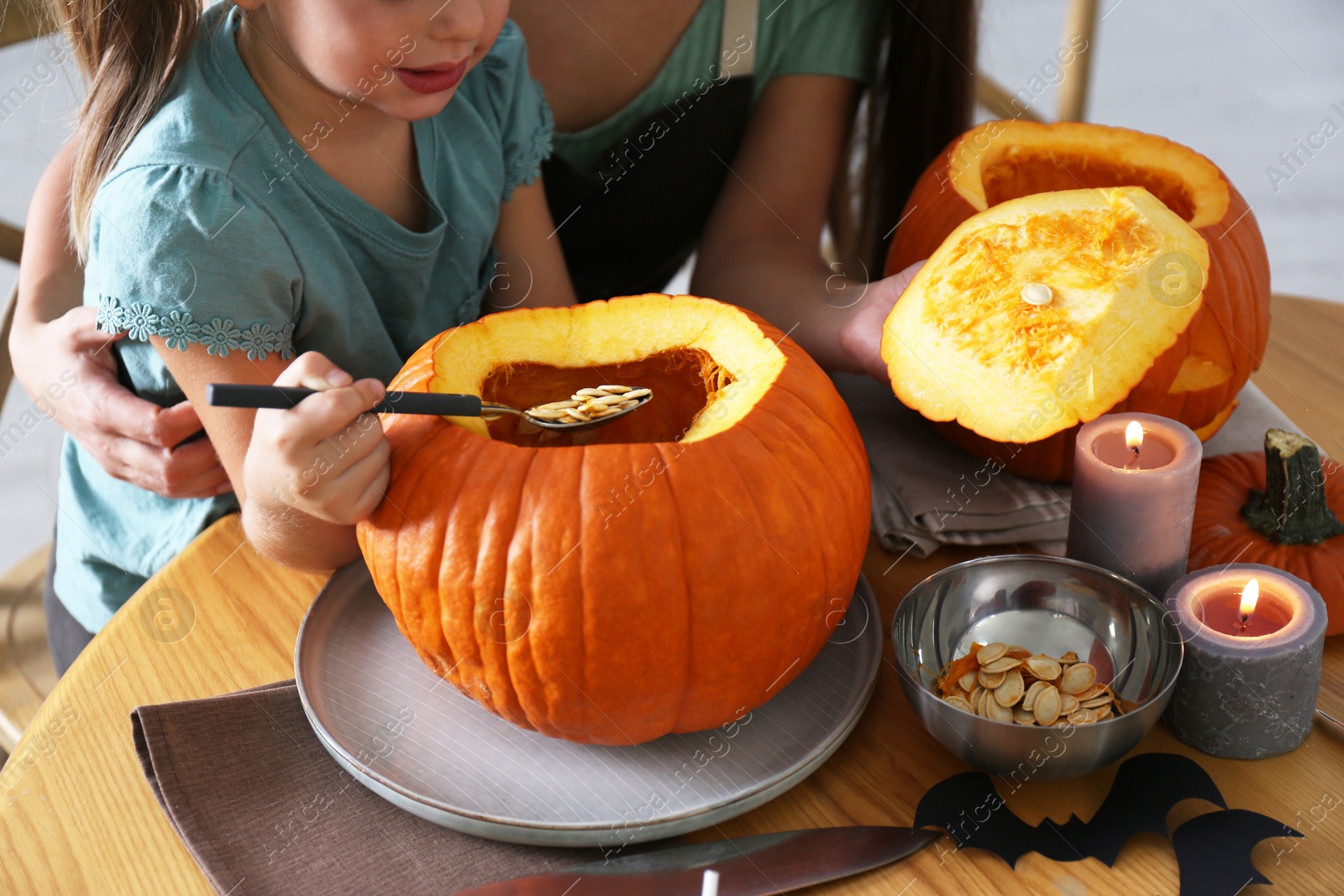 Photo of Mother and daughter making pumpkin jack o'lantern at table, closeup. Halloween celebration