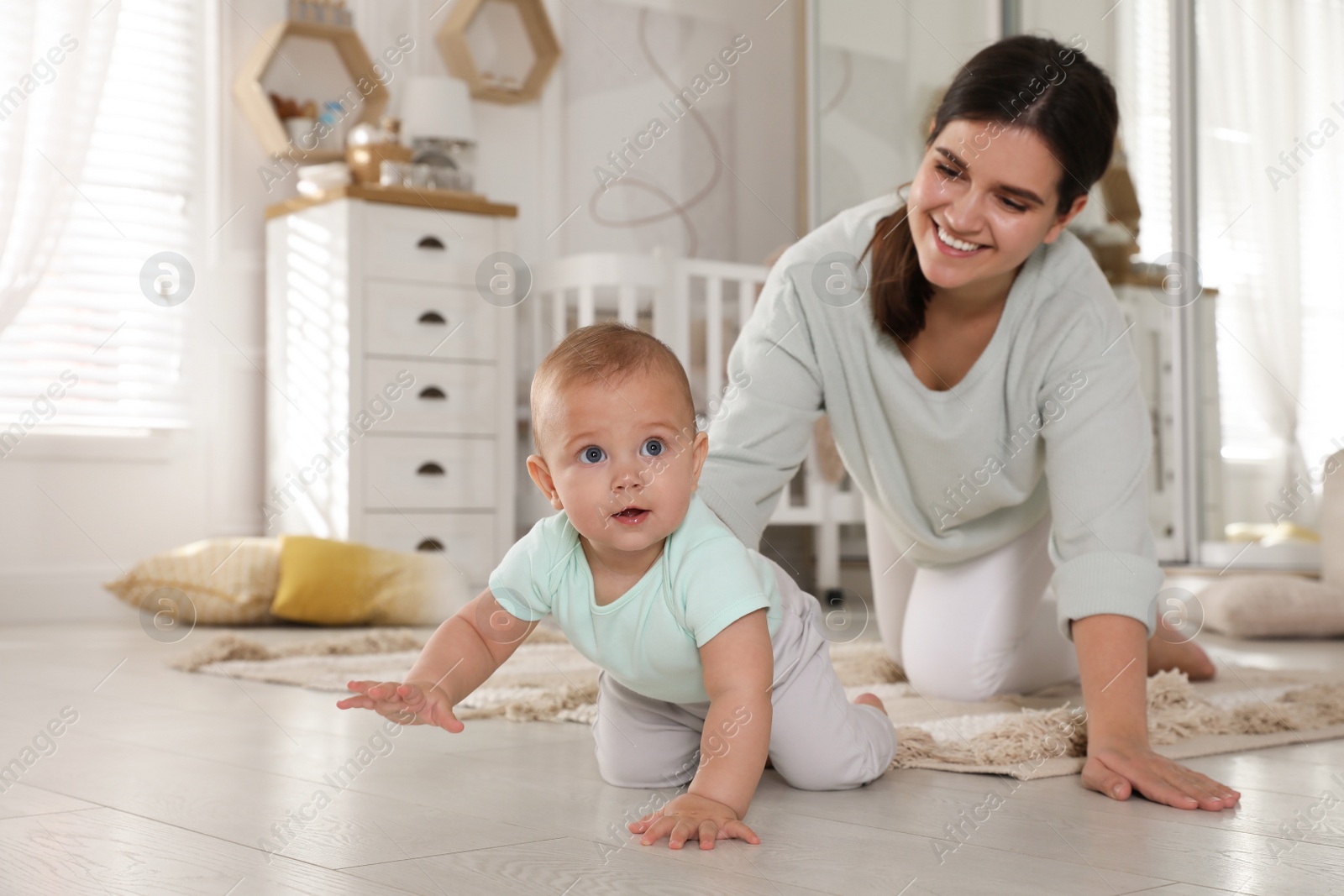 Photo of Happy young mother watching her cute baby crawl on floor at home