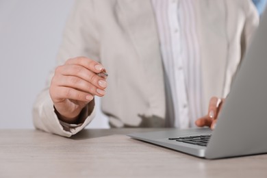 Woman with pen working on laptop at wooden table, closeup. Electronic document management