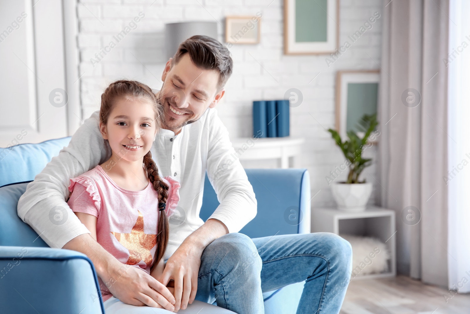 Photo of Dad and his daughter sitting on sofa and hugging at home. Father's day celebration