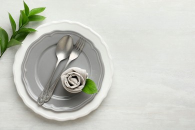 Photo of Stylish setting with cutlery, napkin, branch and plates on light textured table, top view. Space for text