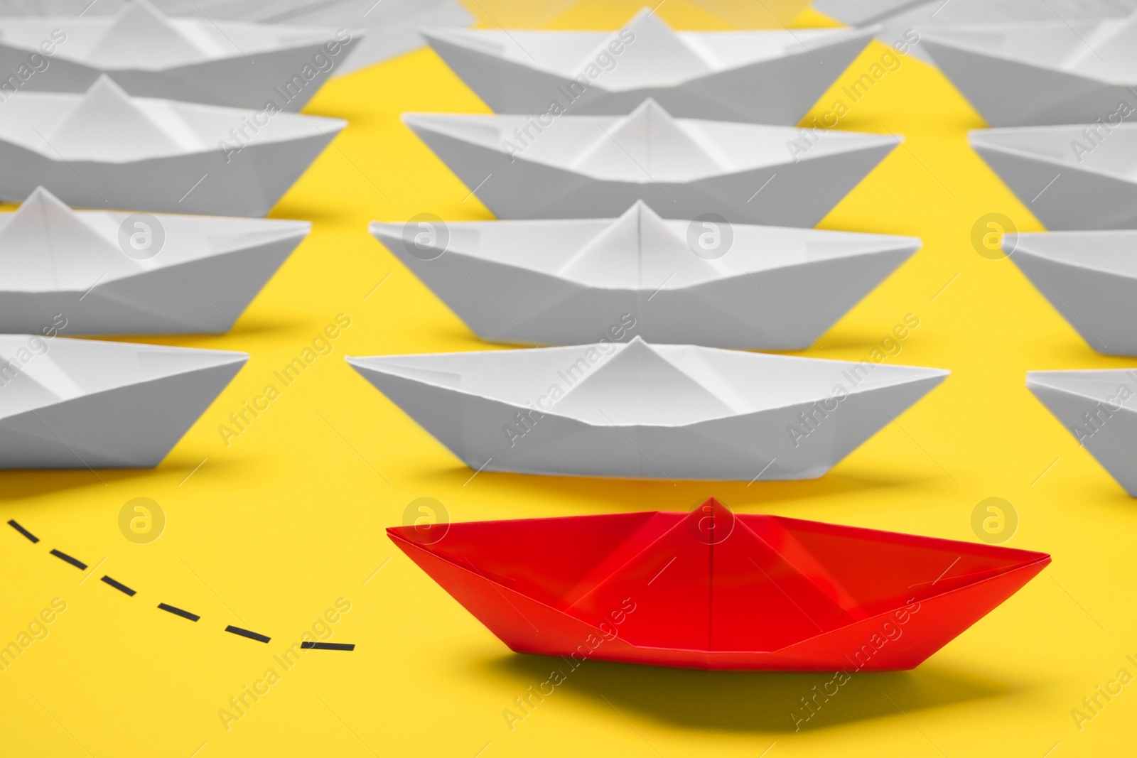 Photo of Red paper boat floating away from others on yellow background, closeup. Uniqueness concept