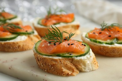 Tasty canapes with salmon, cucumber and cream cheese on table, closeup