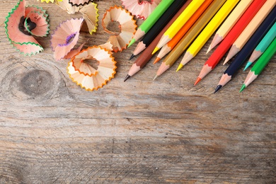 Photo of Color pencils and shavings on wooden table, flat lay. Space for text