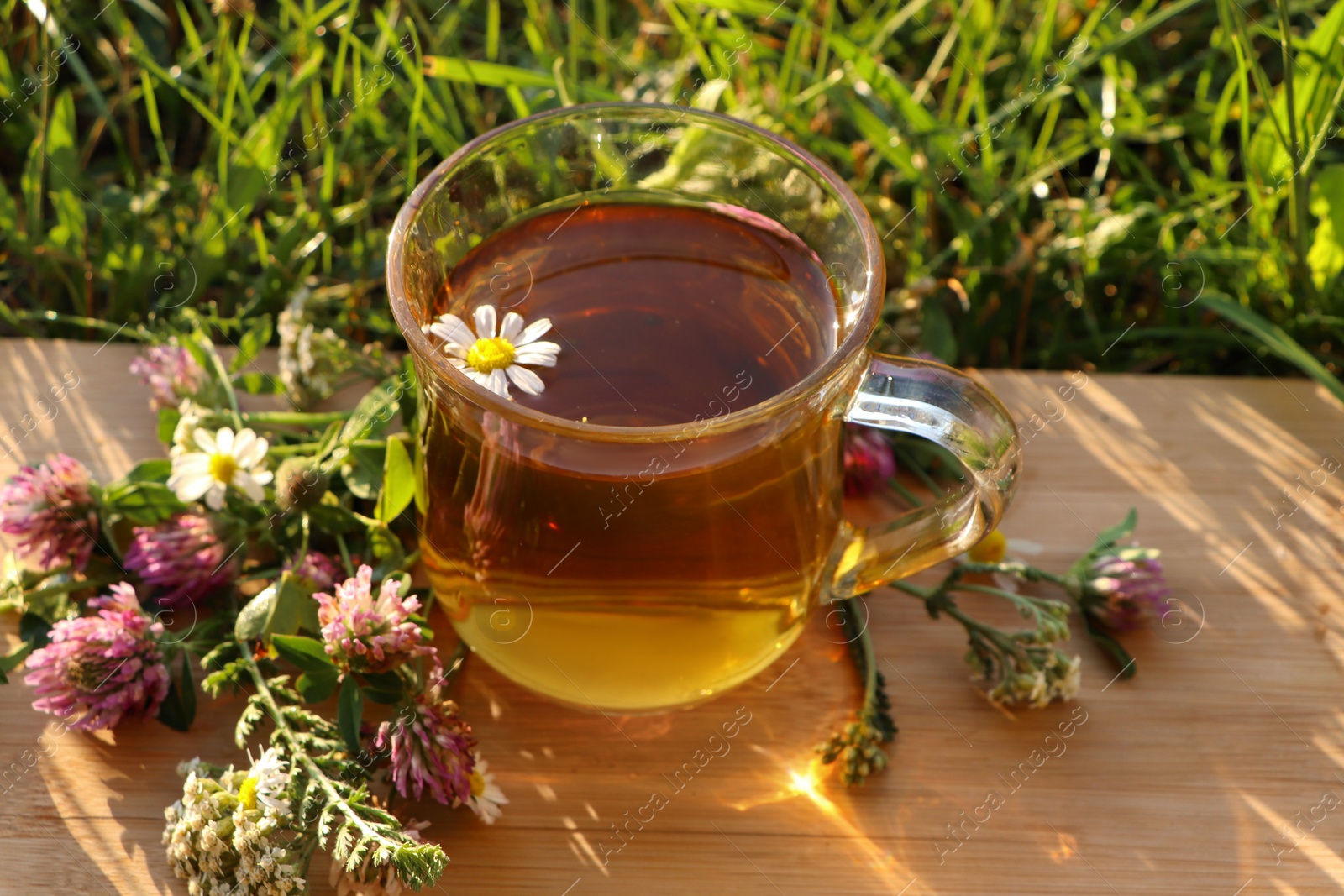 Photo of Cup of aromatic herbal tea and different wildflowers on green grass outdoors, closeup