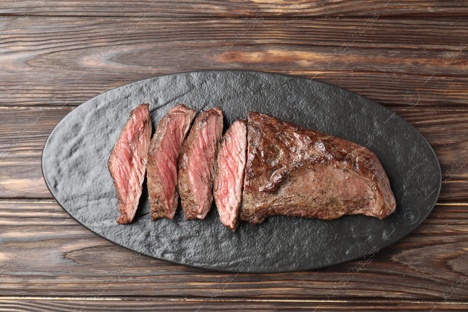 Photo of Pieces of delicious grilled beef meat on wooden table, top view