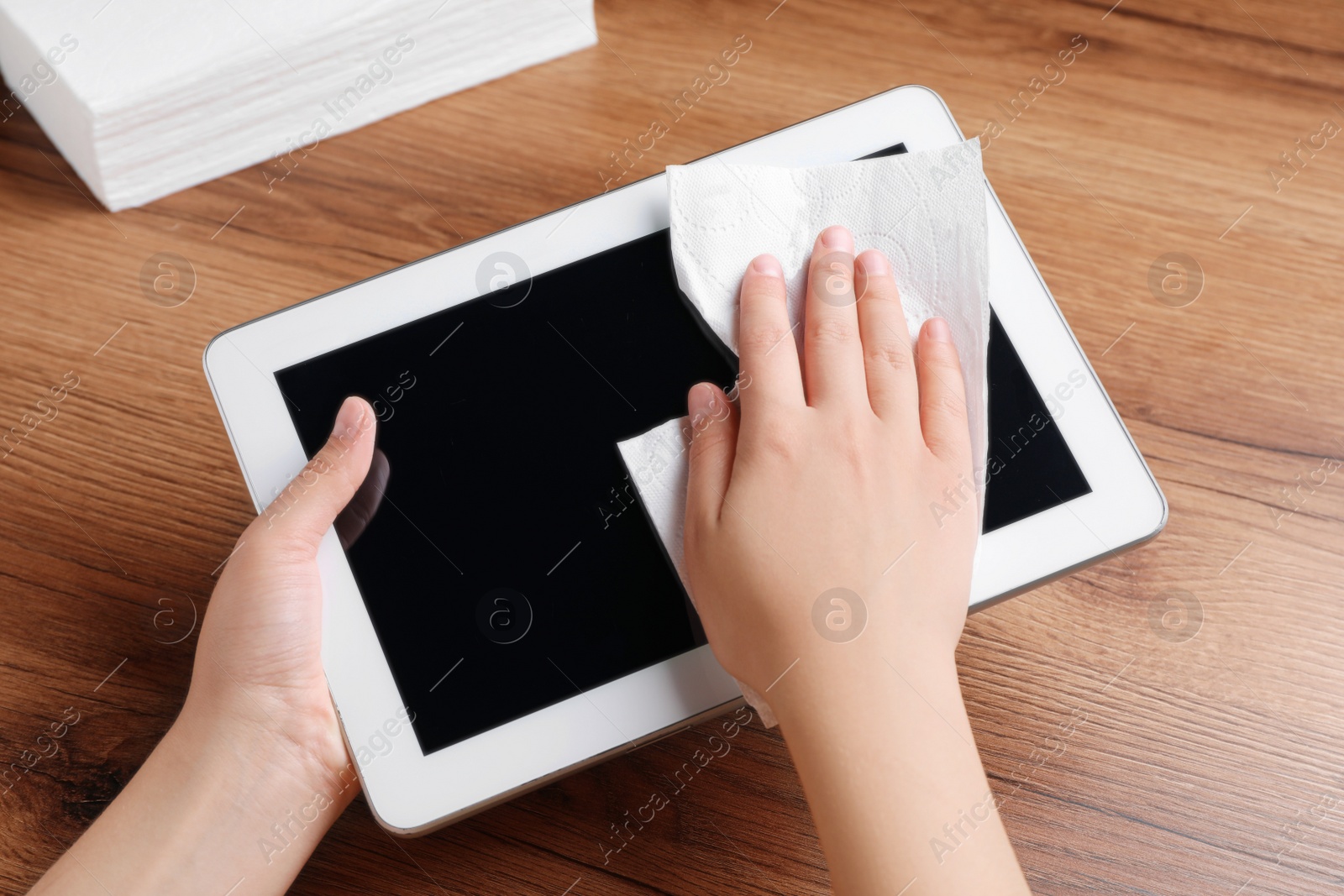 Photo of Woman wiping device with paper towel at wooden table, closeup