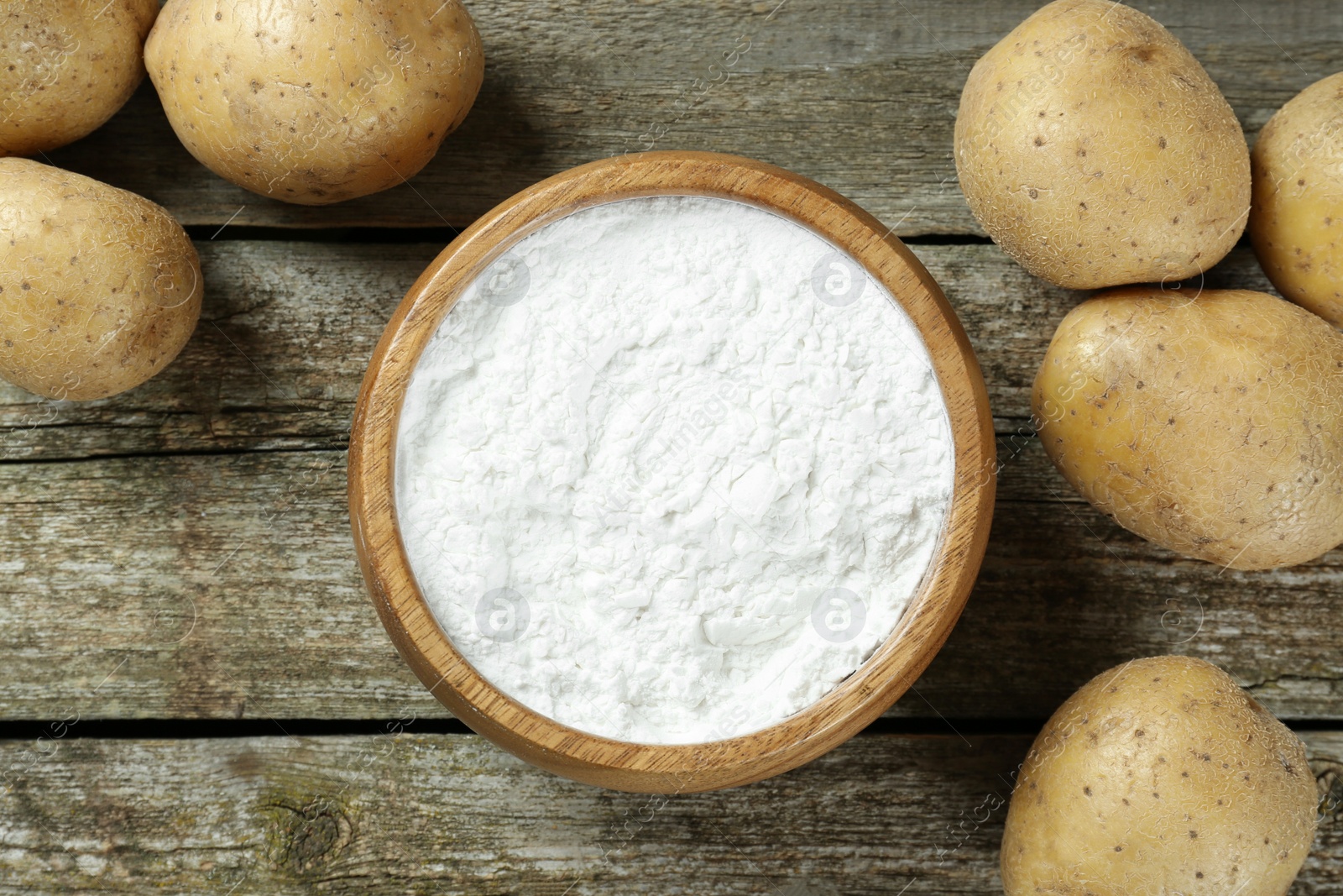 Photo of Bowl with starch and fresh potatoes on wooden table, flat lay