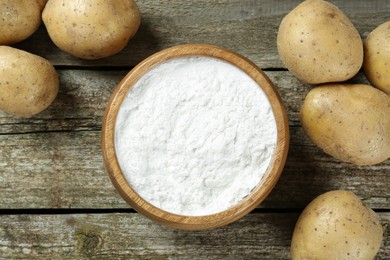 Bowl with starch and fresh potatoes on wooden table, flat lay