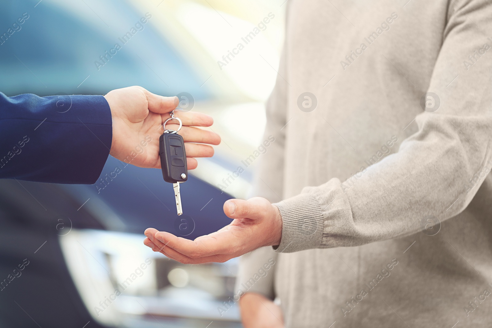 Image of Salesman giving key to customer in modern auto dealership, closeup. Buying new car