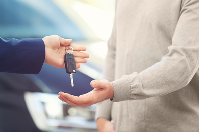 Salesman giving key to customer in modern auto dealership, closeup. Buying new car