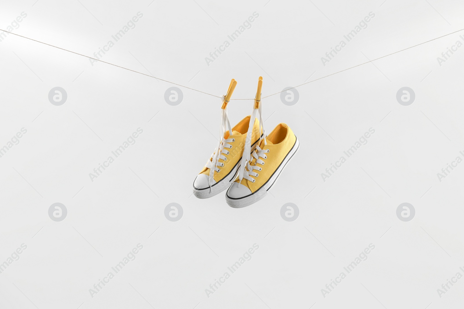 Photo of Stylish sneakers drying on washing line against light grey background