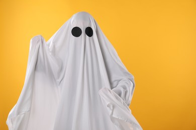 Photo of Creepy ghost. Person covered with white sheet on yellow background, space for text