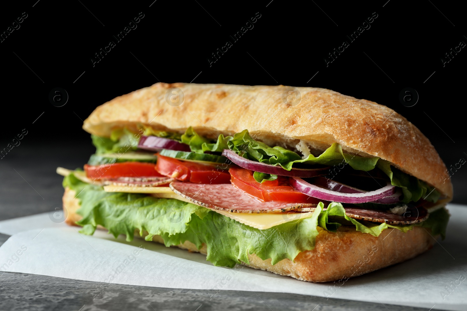 Photo of Delicious sandwich with fresh vegetables and salami on grey table, closeup