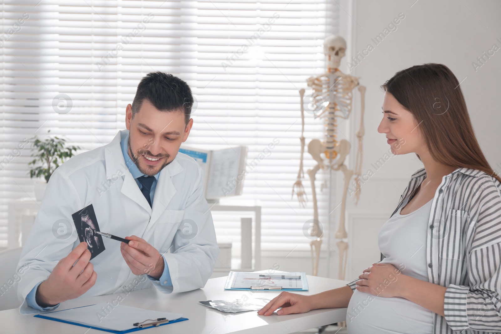 Photo of Gynecologist showing ultrasound picture to pregnant woman in clinic