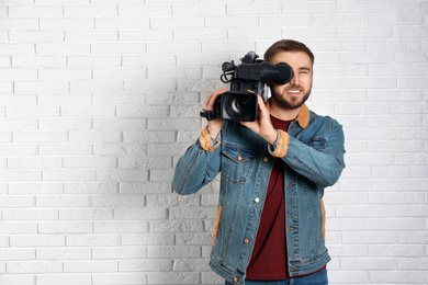 Photo of Operator with professional video camera near white brick wall