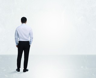 Man standing in front of light marble wall, back view. Space for text