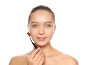 Young woman applying foundation on her face against white background