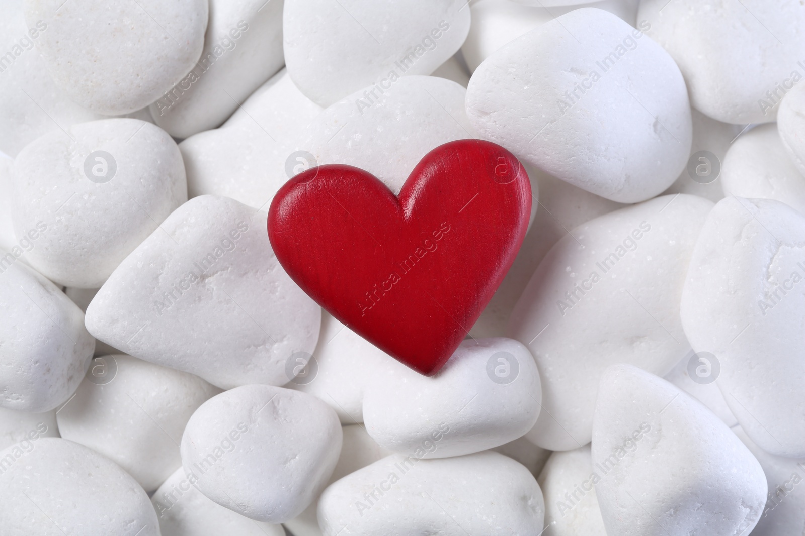 Photo of Decorative heart on white pebble stones, top view