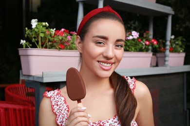 Photo of Beautiful young woman holding ice cream glazed in chocolate on city street