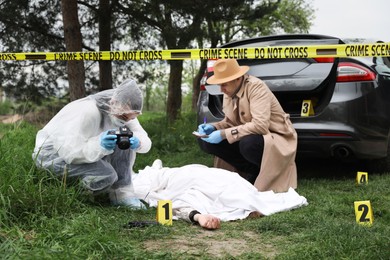 Photo of Investigator and criminologist working at crime scene with dead body outdoors