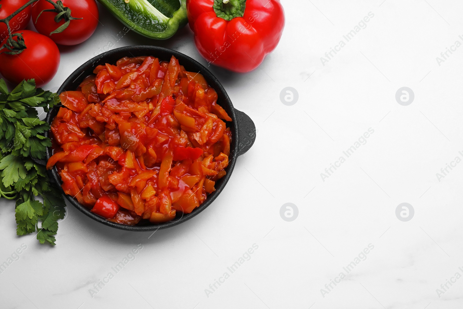 Photo of Delicious lecho in frying pan and ingredients on white table, flat lay. Space for text