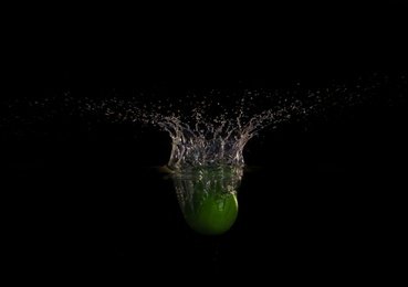 Apple falling down into clear water against black background