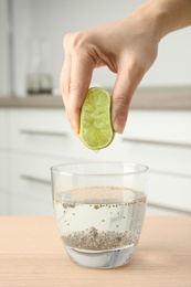 Photo of Young woman squeezing lime into glass of water with chia seeds on table, closeup