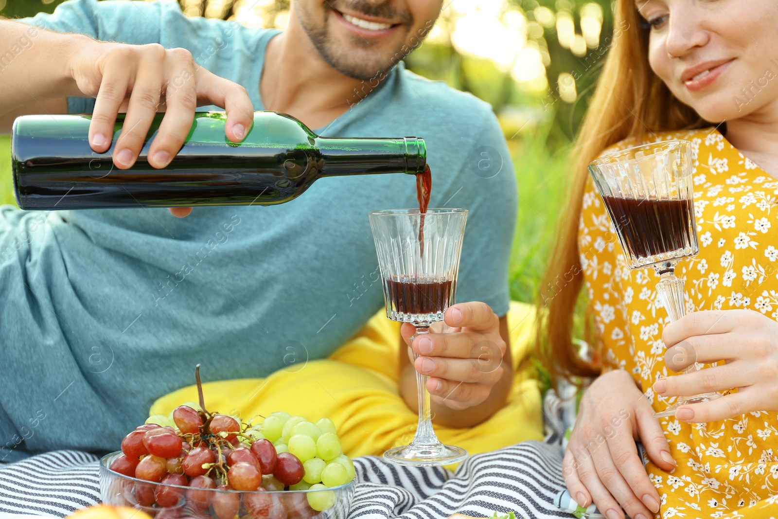 Photo of Young couple with wine and glasses having picnic outdoors, closeup