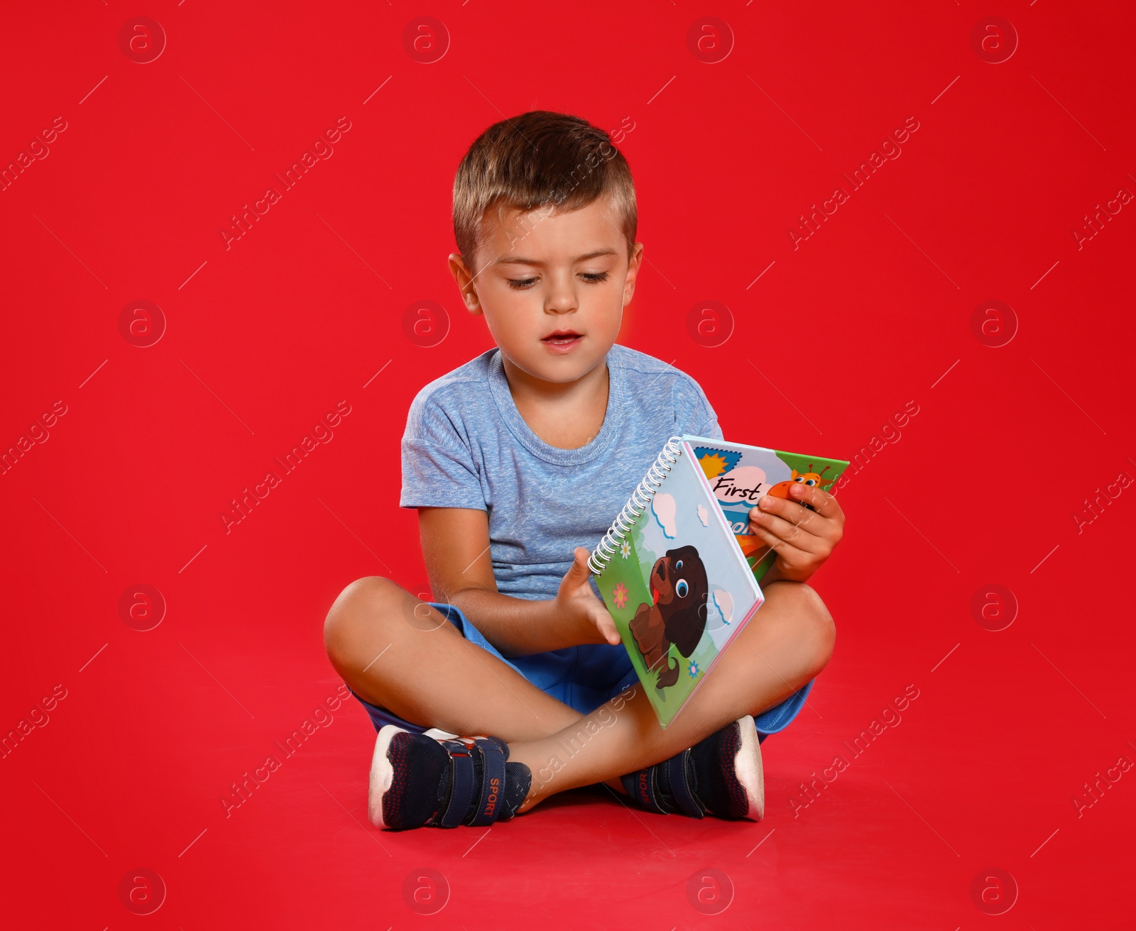 Photo of Cute little boy reading book on red background