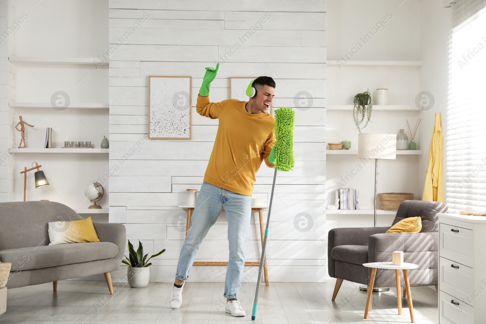 Photo of Man in headphones with mop singing while cleaning at home