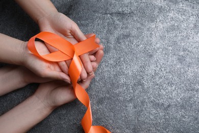 Photo of Couple holding orange ribbon on grey background, top view with space for text. Multiple sclerosis awareness