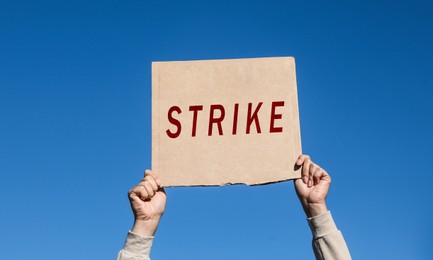 Image of Young woman holding Strike sign against blue sky, closeup