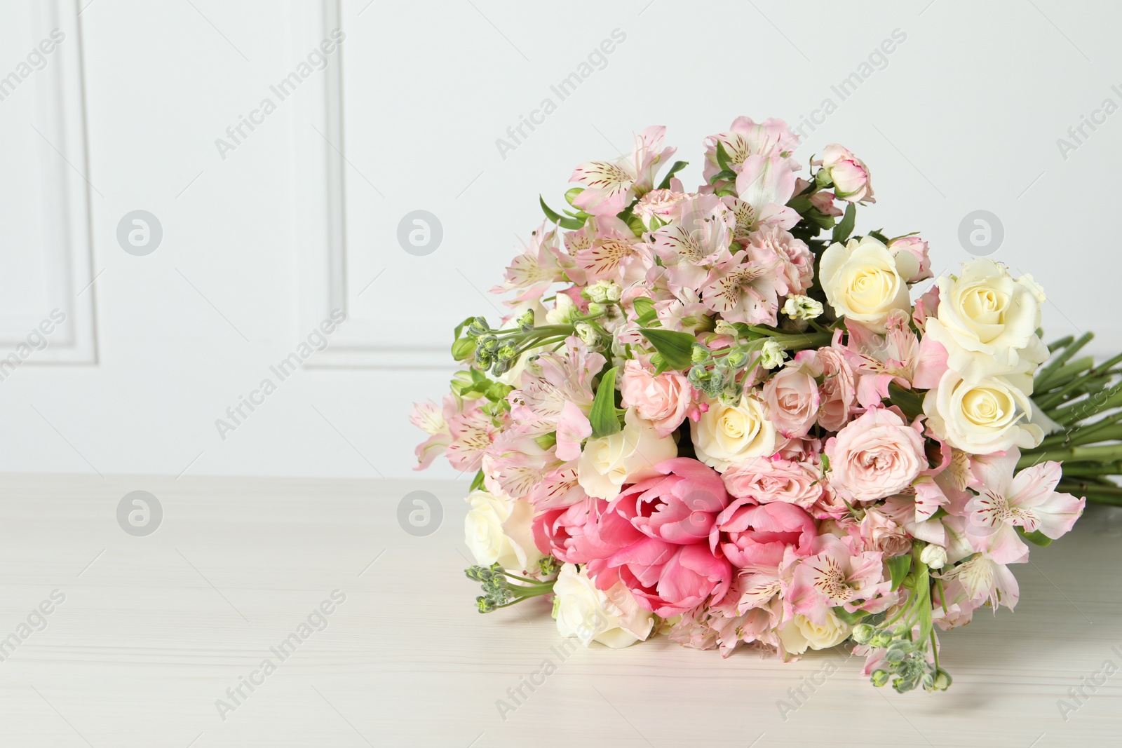 Photo of Beautiful bouquet of fresh flowers on table near white wall. Space for text