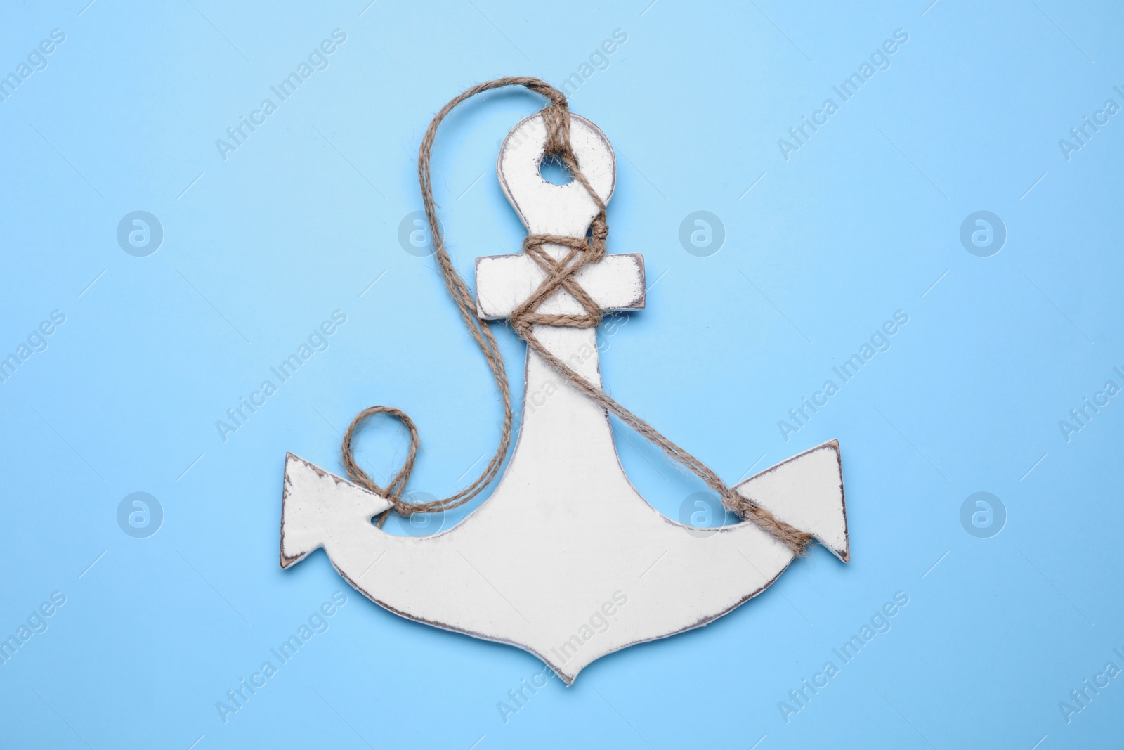 Photo of White anchor with hemp rope on pale blue background, top view